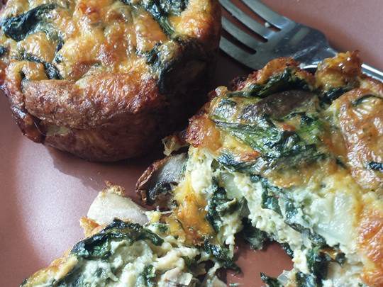 two spinach mushroom crustless mini quiches, one split open with a stainless steel fork behind it on a plate