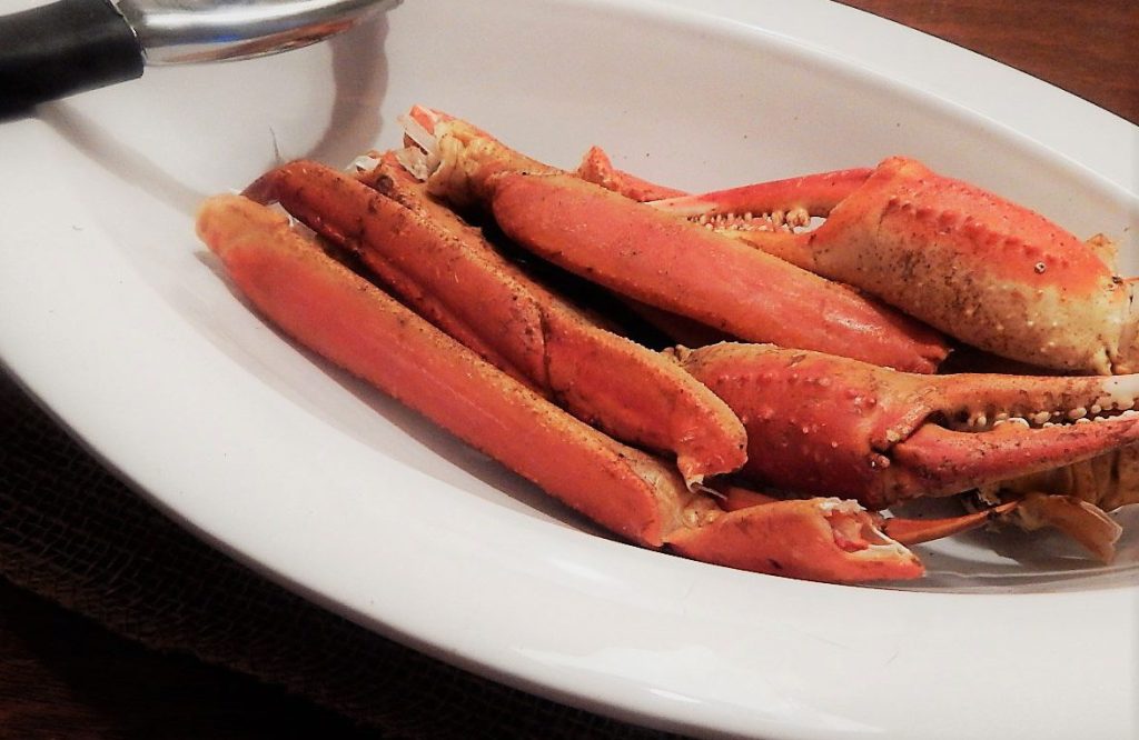 steamed crab legs in an oval white bowl with a seafood cracker