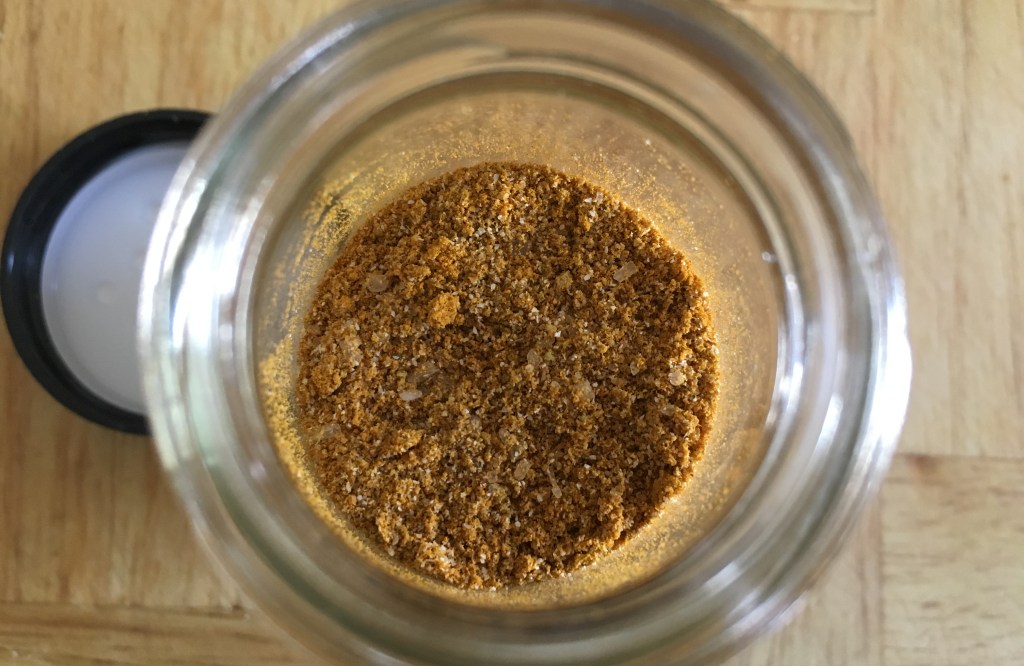 sazon in an open glass spice jar on a wooden surface