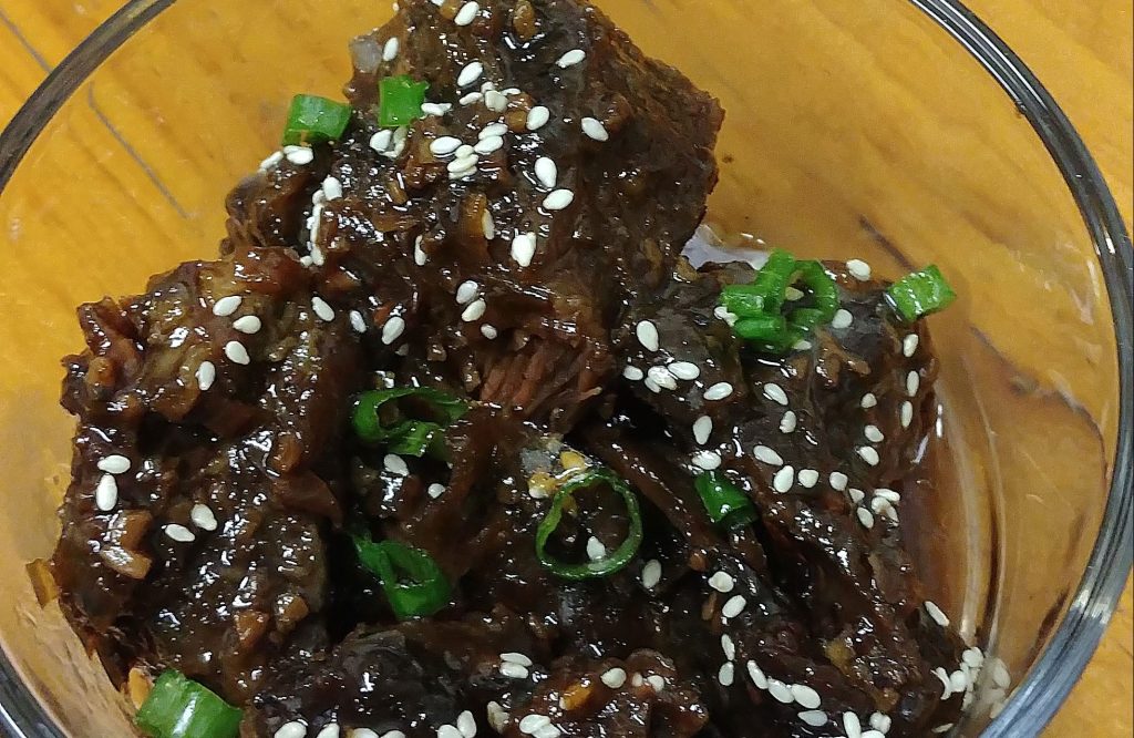 Korean-style short ribs in a glass bowl on a wooden surface
