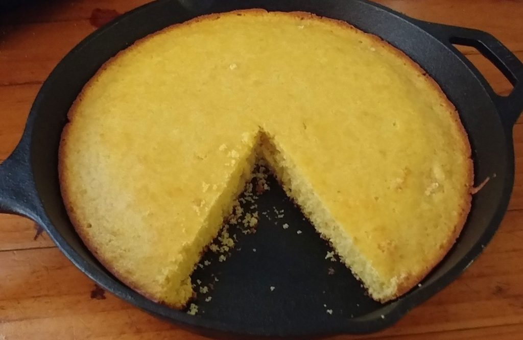 sweet cornbread, with a slice removed, in a cast-iron skillet on a wooden surface