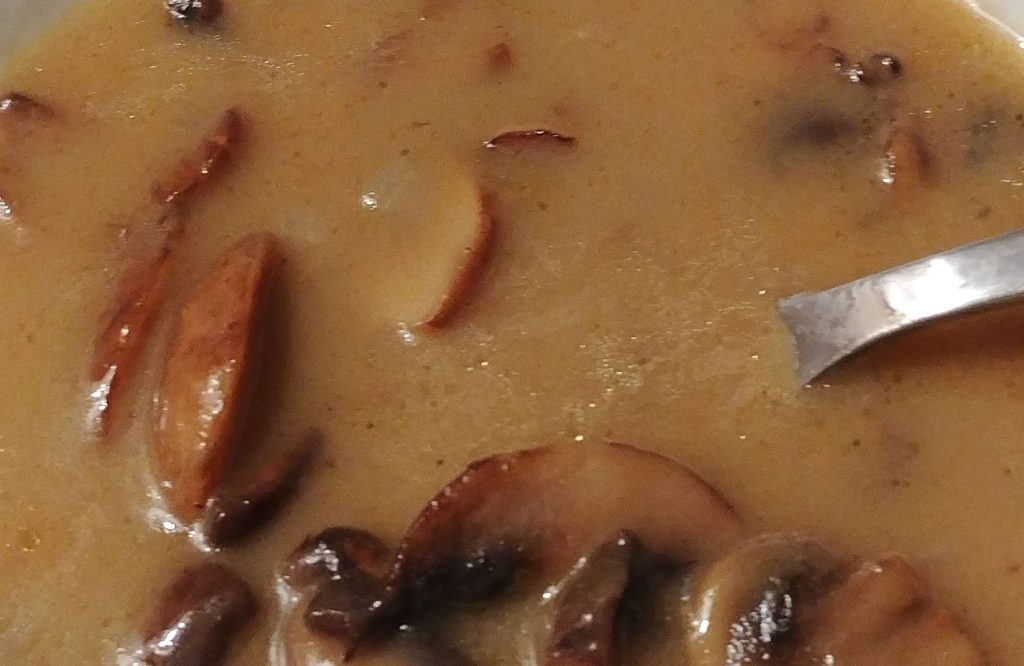 a bowl of mushroom soup with a stainless steel spoon in it