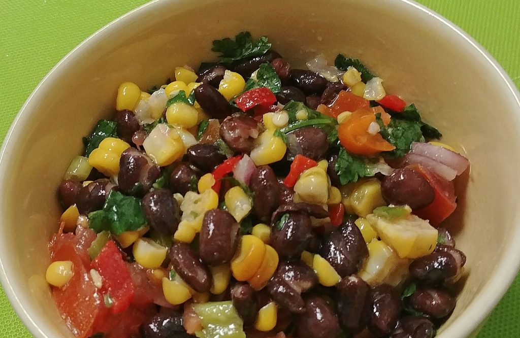 corn and black bean salad with garlic lime dressing in a bowl on a green surface