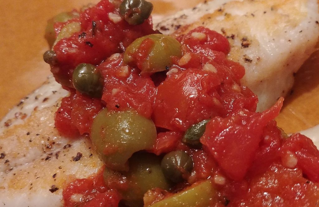 snapper with tomatoes, olives, and capers on a yellow plate