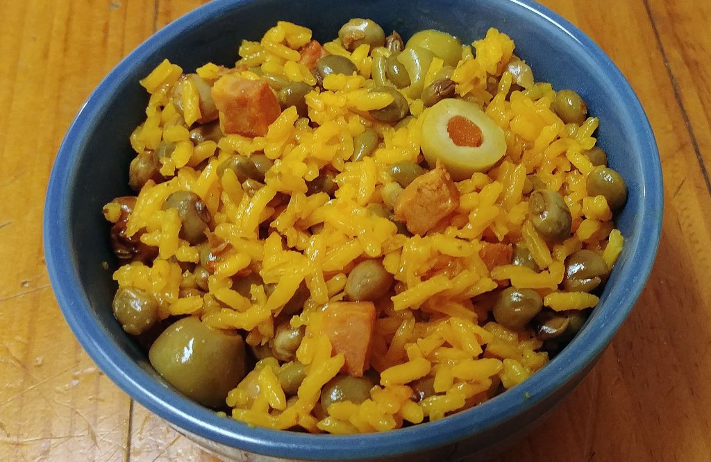 Spanish rice with pigeon peas (arroz con gandules) in a blue bowl on a wooden counter