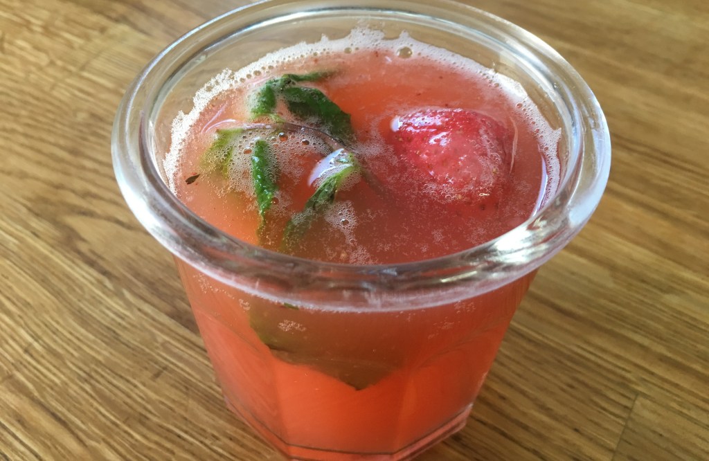 glass of agua de fresa (aguas frescas) garnished with mint and a strawberry on a wooden surface